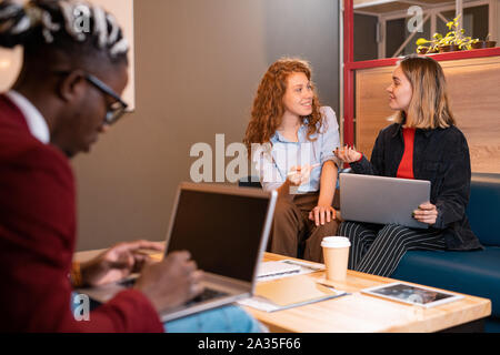 Two young happy casual businesswomen or students discussing working moments Stock Photo