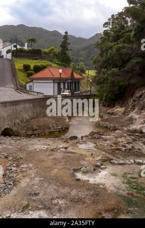 River from the hot sulphur springs, among a road and a forest. Building in the background. Area of the famous spa. Furnas, Sao Miguel, Azores Islands, Stock Photo