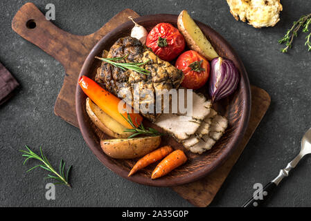 Oven Roasted Meat and Vegetables. Roast Pork Dinner with seasonal vegetables and herbs on black background, top view. Stock Photo