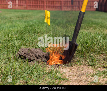 Real black smoke and flames rise from fire in hole of yard. Yellow natural gas warning sign, plastic pipe, shovel. Concept of notify utility company Stock Photo