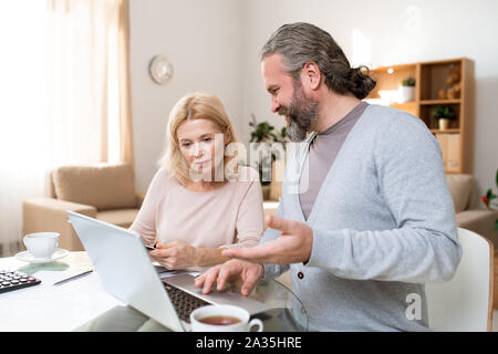 Two mature colleagues discussing online data or preparing presentation Stock Photo