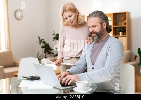 Happy mature couple looking at laptop display while one of them entering data Stock Photo