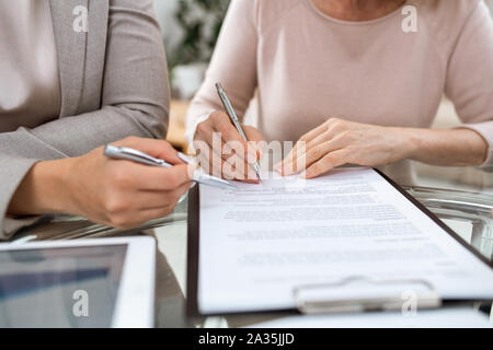 One of two businesswomen with pens going to put signature on page of contract Stock Photo