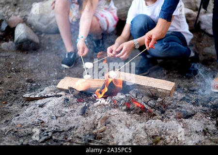 Teenagers, sitting around the fire, fry a banana on a stick Stock Photo