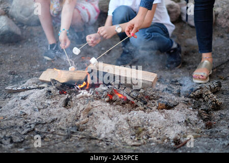 Teenagers, sitting around the fire, fry a banana on a stick Stock Photo