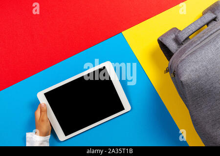 Top view to kid hands with tablet computer and gray backpack on colorful background Stock Photo