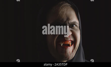 Vampire Halloween man portrait. Guy with dripping blood on his face. Executioner, Vampire makeup. Fashion art design. Attractive model in Halloween costume. Dark black background Stock Photo