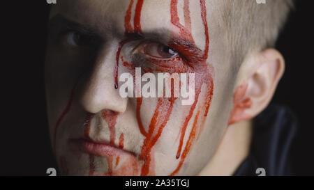Halloween man portrait with head injury. Guy with dripping blood on his face close-up. Man after fight makeup. Fashion art design. Attractive model in Halloween costume. Dark black background Stock Photo