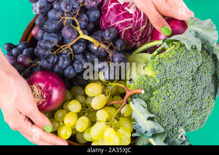 Woman's hands holdinh dish with fresh autumn produce - dark and white grapes, broccoli, red onions and chicory. Green clean eating Stock Photo
