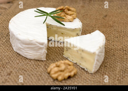 Camembert cheese with herbs, decorated with a sprig of rosemary and walnut. Close-up. Stock Photo