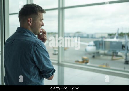 Caucasian young man is afraid to flight standing in terminal near window Stock Photo