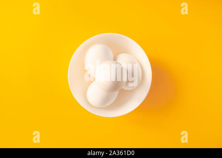 Four white eggs in a bowl on yellow background. Stock Photo