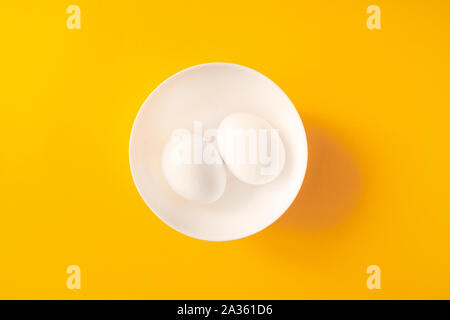 Two white eggs in a bowl on yellow background. Stock Photo