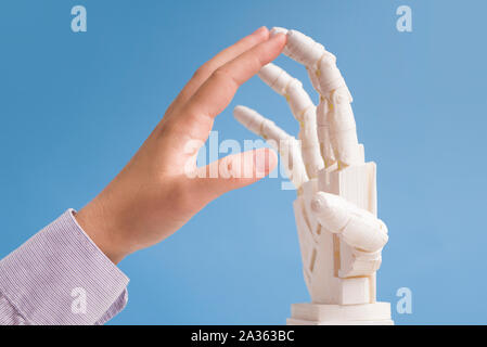 Human and robot hands touching each other, blue background Stock Photo