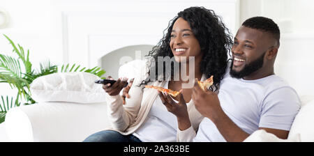 Cheerful black man and woman having pizza and watching tv. Stock Photo