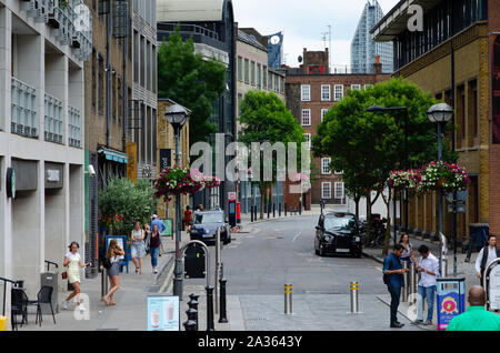 Beautiful London street with flowers, people, green trees and parked black cab. Photo shows 'New Globe walk' street, near Shakespeare's Globe Theatre Stock Photo