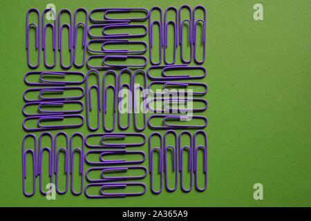 Purple paperclips in a geometric pattern on a green background with an isolated red and yellow paperclip to one side Stock Photo
