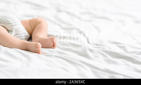 Closeup of infant baby feet lying on bed in bodysuit Stock Photo