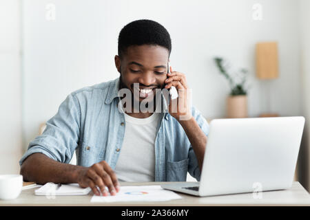 Cheerful african businessman checking financial reports and talking on phone Stock Photo