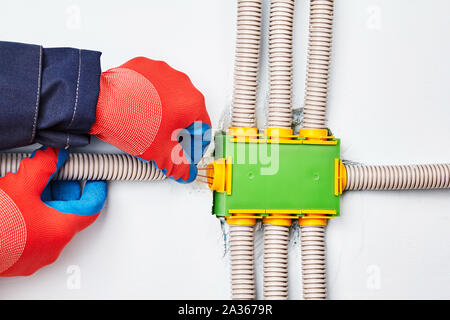 An electrician connects an electric conduit to a square-shaped distribution box made of green plastic and containing eight ways. The rectangular junct Stock Photo