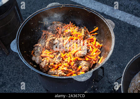 Juicy appetizing pieces of meat cooking in a large cauldron with carrot over hot charcoals Stock Photo