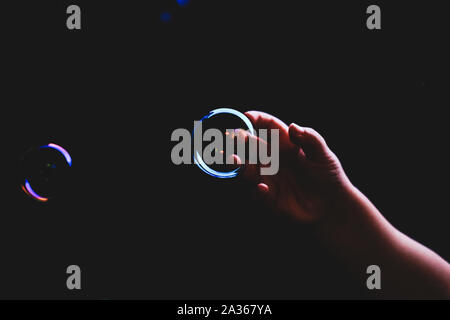 Colorful soap bubbles flying over darck background and human hand tryimg to catch them