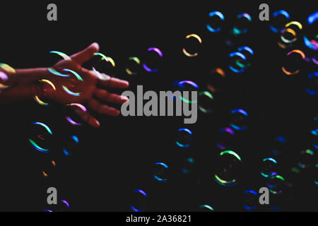 Colorful soap bubbles flying over darck background and human hand tryimg to catch them