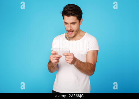 Concentrated young man playing on smartphone, blue background Stock Photo