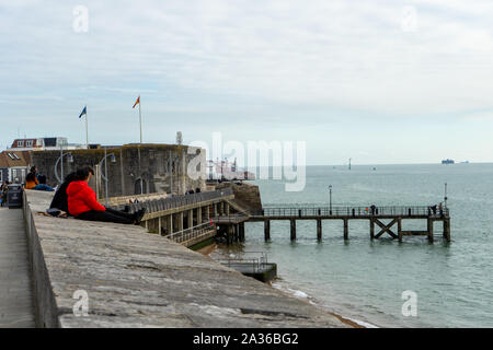 A couple sat talking sitting on the walls at Old Portsmouth looking out to sea Stock Photo