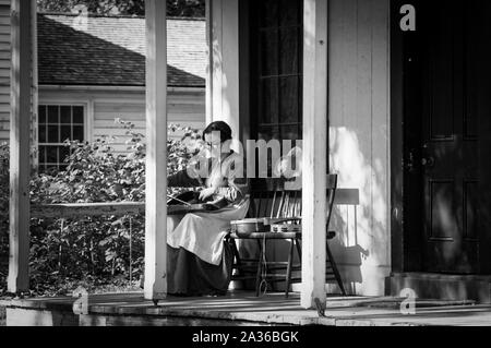 Toronto, Canada - 2019 08 24: A woman wearing 19th century style costume packs her violin into the case on the porch of the old wooden house in the Stock Photo
