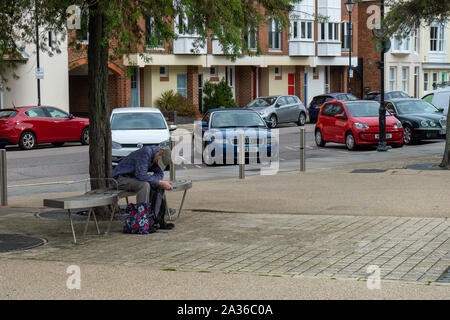 A man sitting alone on a bench holding his head looking depressed Stock Photo