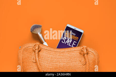 Happy Halloween Sale background concept for cosmetic and bag. Wicker bamboo handmade weave handbag with smartphone and make-up brush inside. Stock Photo