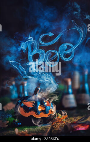 Halloween concept with a ceramic pumpkin and Boo lettering made out of the smoke. Creative autumn still life on a dark background Stock Photo