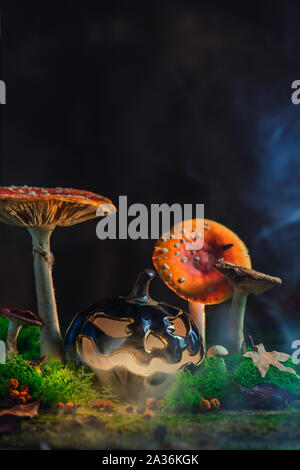 Spooky Halloween concept with a ceramic pumpkin among poisonous mushrooms. Creative autumn still life with DIY on a dark background Stock Photo