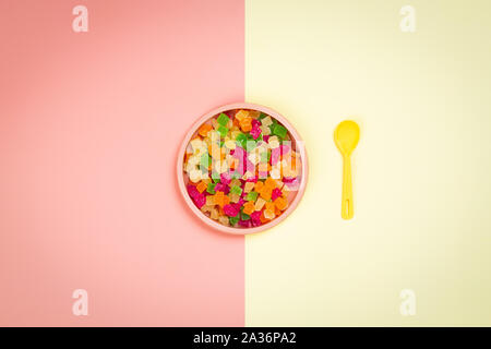 Minimalistic flat lay with a plastic pink plate with dried slices of candied pineapple and a yellow spoon in a yellow-pink isolated background. Plasti Stock Photo