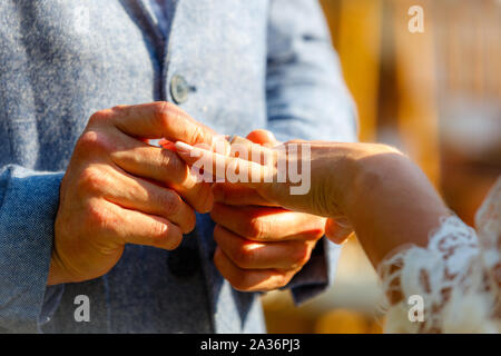 Groom putting a white gold wedding ring with diamonds on brides finger. Wedding ceremony. Sunny day. Stock Photo