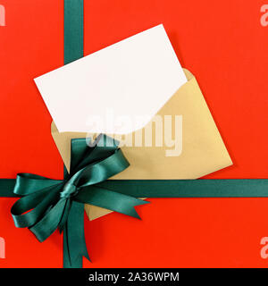 Open Christmas or birthday card with green gift ribbon bow on plain red background paper, copy space, vertical Stock Photo
