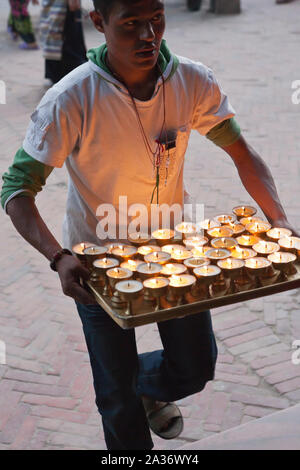 Nepali man carries burning oil lamps near Buddhist stupa of Bodhnath (Boudha) in Kathmandu Nepal Stock Photo