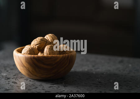 inshell walnuts in olive wood bowl on terrazzo countertop, shallow focus Stock Photo