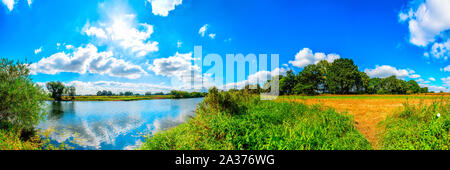 Landschaft am Flussufer mit Feldern und Bäumen bei blauen Himmel mit Sonnenschein Stock Photo