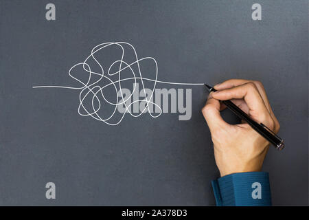 The way to business thinking success concept. A businessman hand drawing a white tangle line on blackboard. Stock Photo