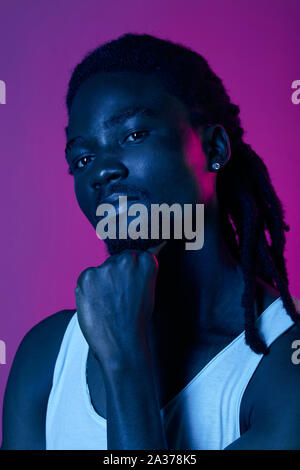 arrogant bearded confident afro man with earring leaning on his fist looking at the camera, isolated blue and purple baackground Stock Photo