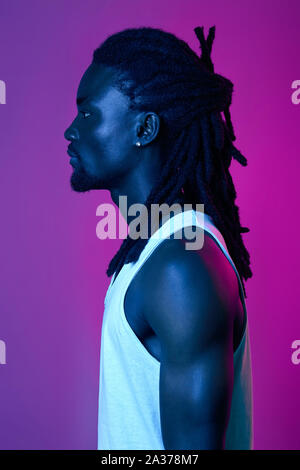 profile of handsome Afro guy with stylish dreads, close up side view portrait, stylish and fashion concept. isolated pink and violet background Stock Photo