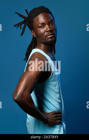 african guy with beautiful hairstyle holding hands on the hips and posing to the camera, close up photo.isolated blue background. Stock Photo