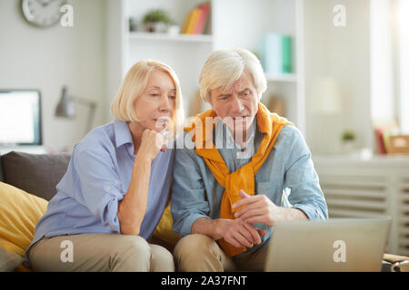 Portrait of modern mature couple using laptop at home, focus on frowning senior man looking t computer screen, copy space Stock Photo