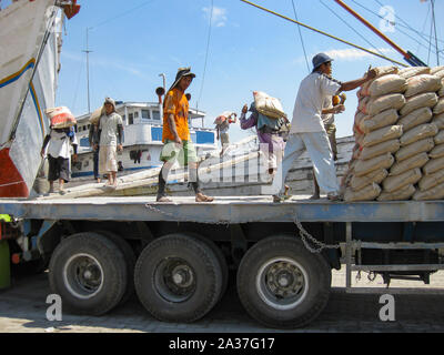 Jakarta, Indonesia - July 13, 2009: unskilled workers loading sacks with cement from a truck onto a wooden transport vessel Stock Photo