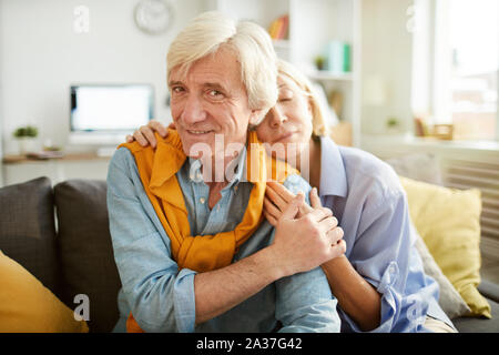 Portrait of loving senior couple embracing sitting on comfortable couch at home, copy space Stock Photo