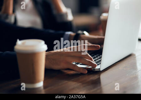 close up cropped photo young mana using laptop at coffee shop, young male student typing on computer sitting at wooden table. man sendinge-mail, messa Stock Photo