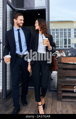 cheerful romantic couple looking at each other holding disposable cups, walking in the city, love, friendship Stock Photo