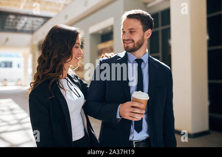 smiling woman putting her hand on her colleague's shoulder, flirting with him, making eyes Stock Photo